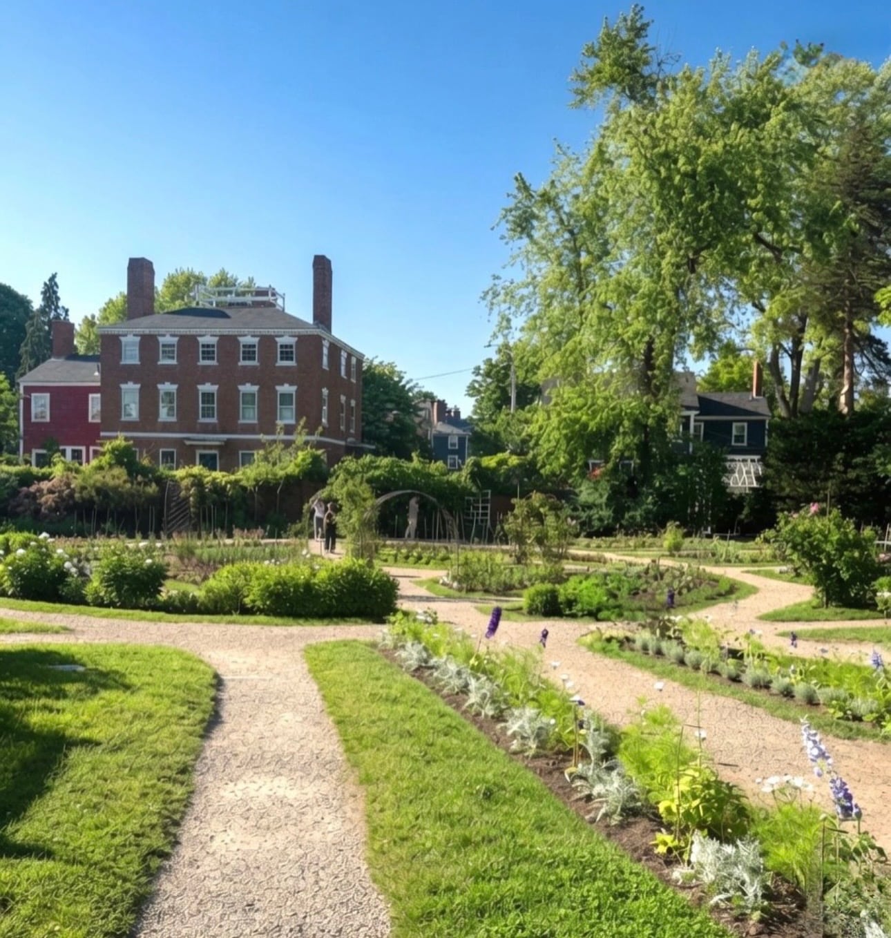 A formal garden with gravel paths and flower beds in front of a grand three-story brick Federal mansion in Salem