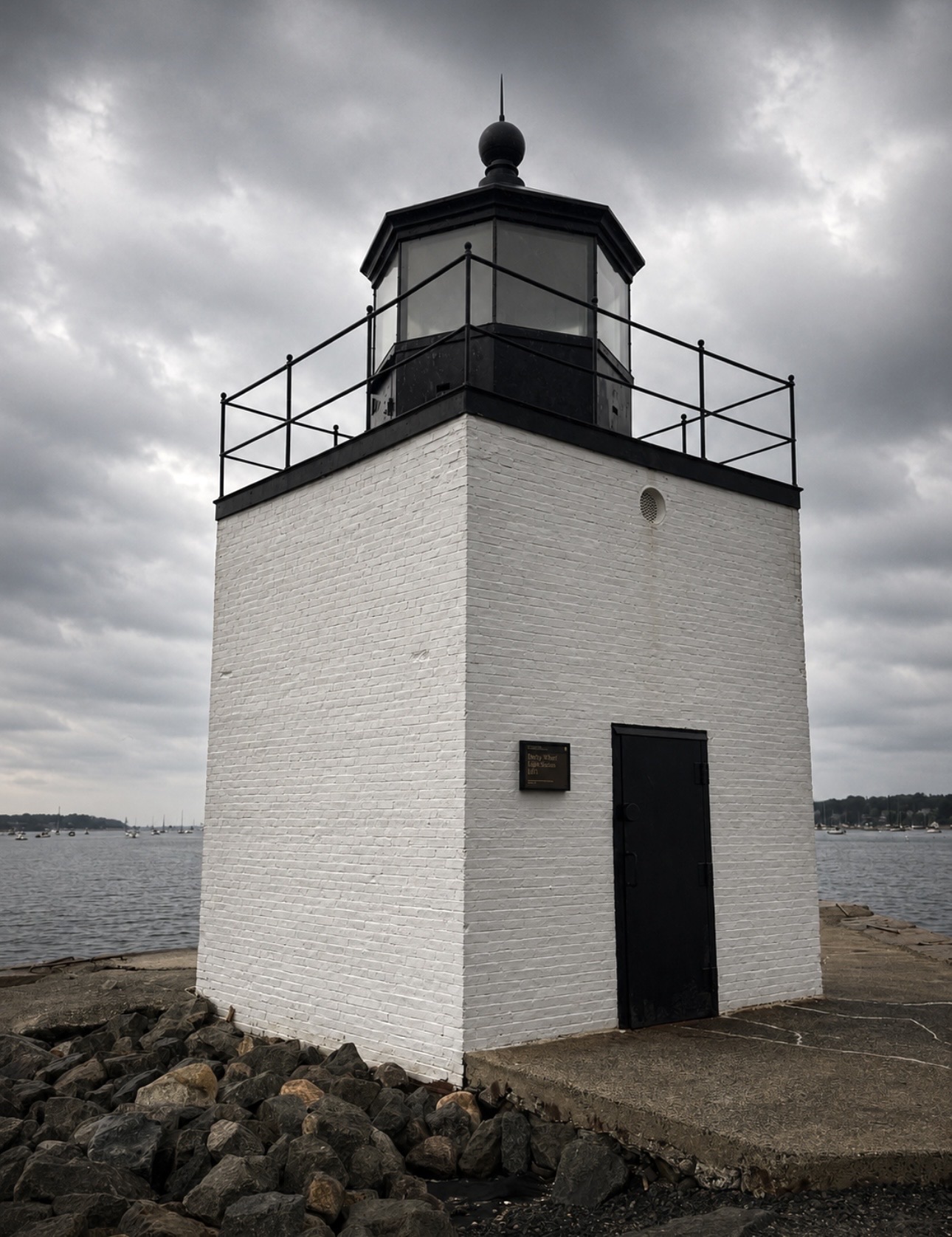 Front view of Derby Wharf Light Station, a square white brick lighthouse with a black lantern room, under moody clouds, Salem MA