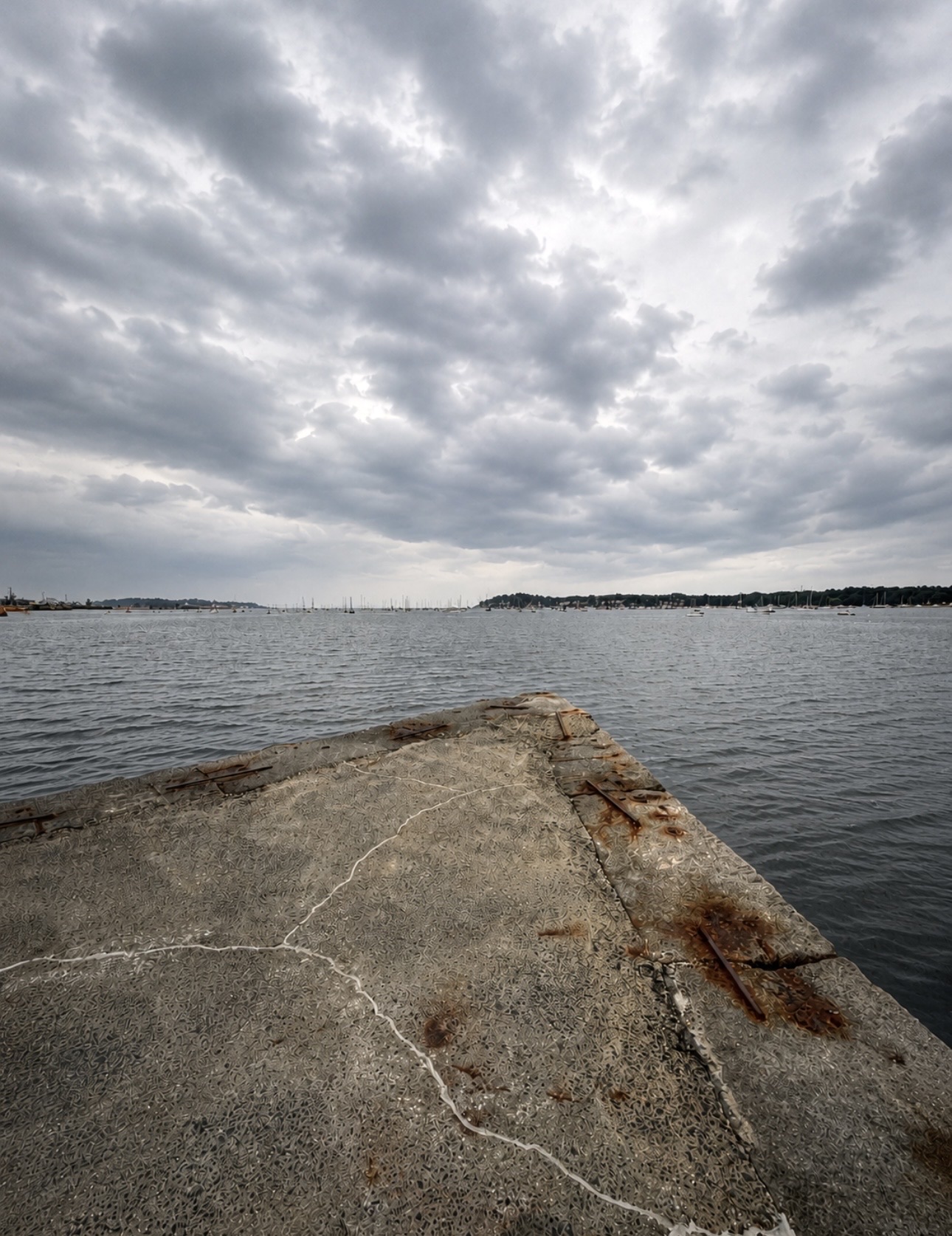 Weathered concrete pier jutting into Salem Harbor under dramatic storm clouds, sailboats moored in the distance, Salem MA