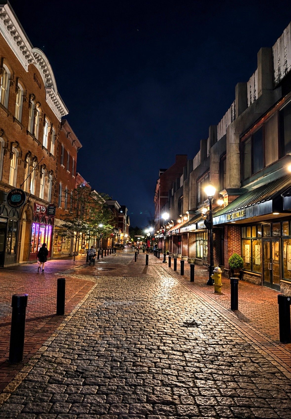 The cobblestone Essex Street pedestrian mall in downtown Salem lit by street lamps and shop windows at night