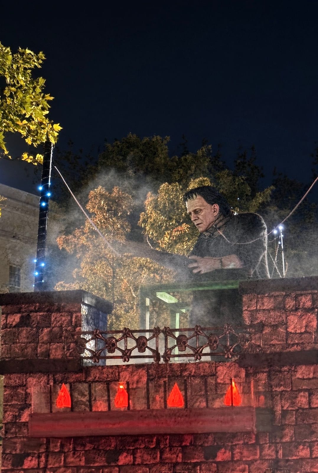 Frankenstein's monster rising from the battlements of a red-lit stone castle float, fog and strings of blue lights around him, against the night sky at the Grand Parade