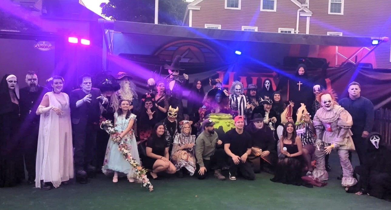 About twenty performers in horror costumes — Frankenstein’s monster, Beetlejuice, Pennywise, Ghostface, Michael Myers, a nun and a witch among them — posed in two rows under purple stage lights