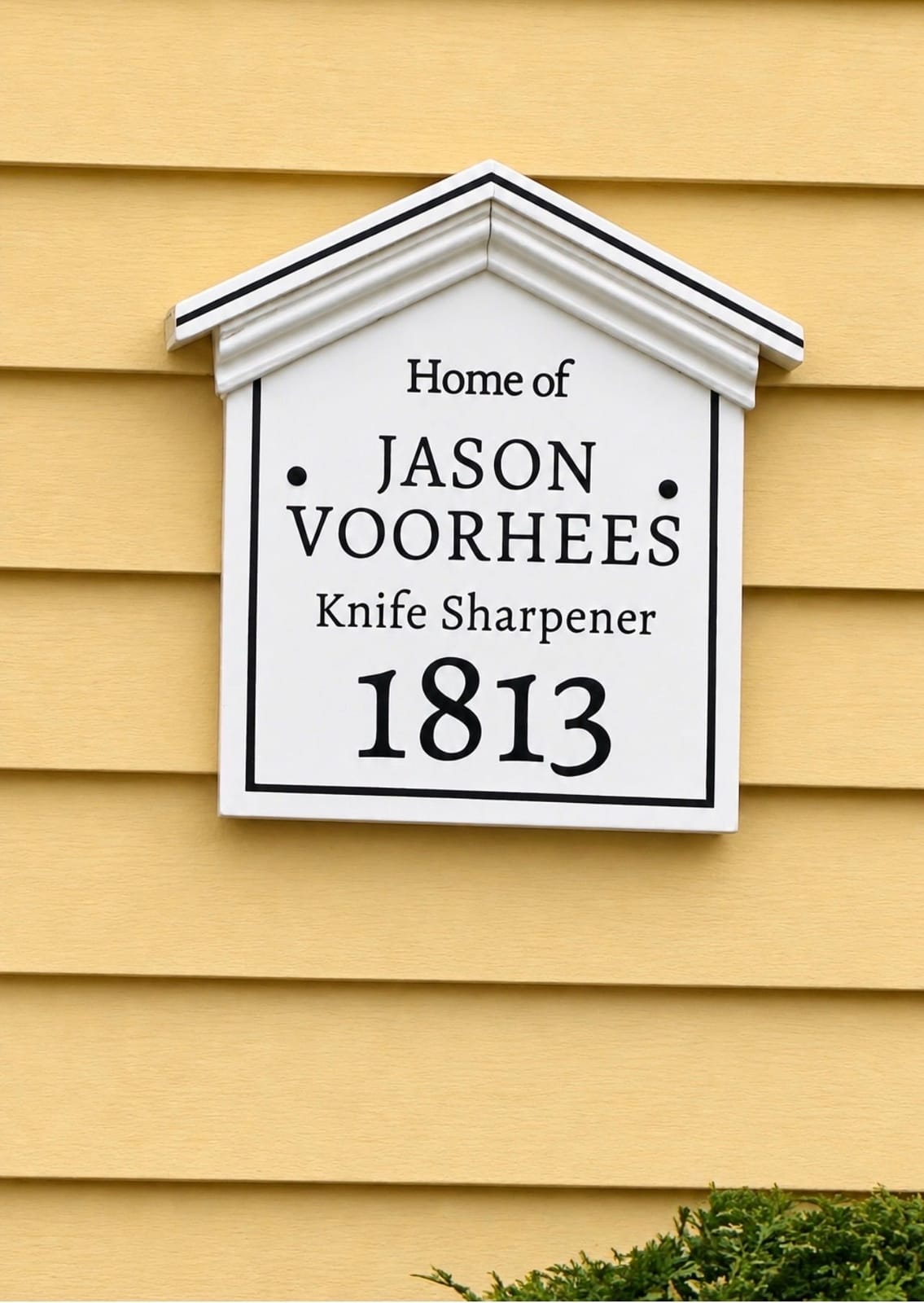 A white peaked house plaque in the style of Salem’s historic home markers, mounted on yellow clapboard siding, reading "Home of JASON VOORHEES, Knife Sharpener, 1813"