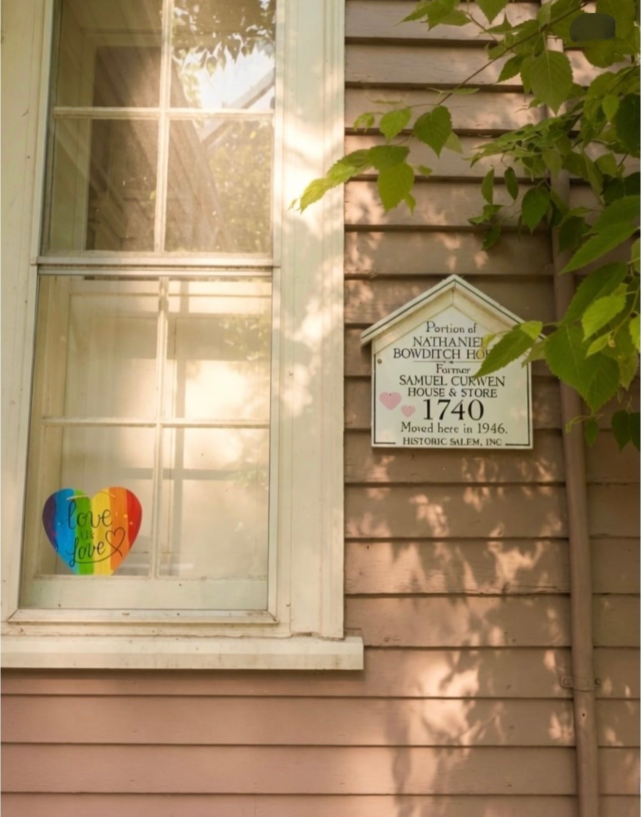 A rainbow 'love is love' heart in a window beside a Historic Salem plaque for a portion of the Nathaniel Bowditch House, formerly the Samuel Curwen House & Store, 1740
