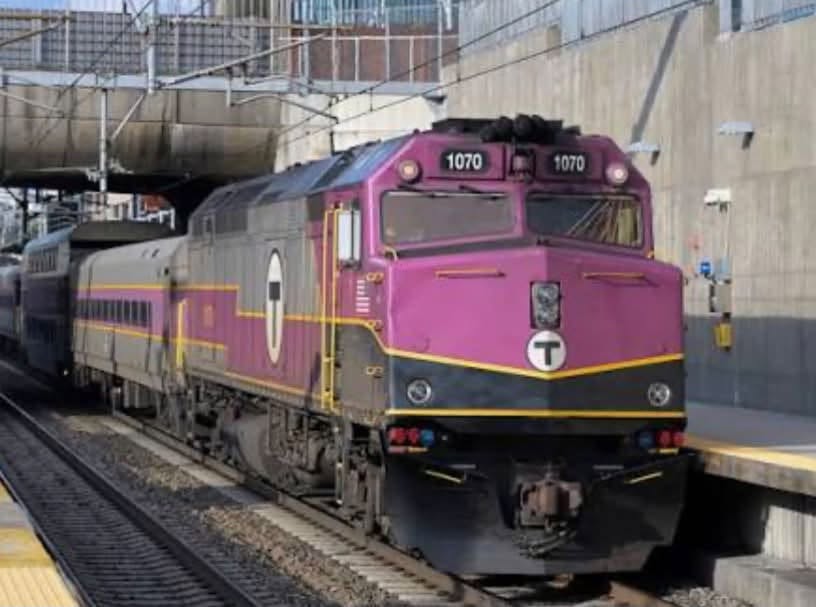 A maroon MBTA commuter rail train (locomotive 1070) pulling into a station platform in the Boston area