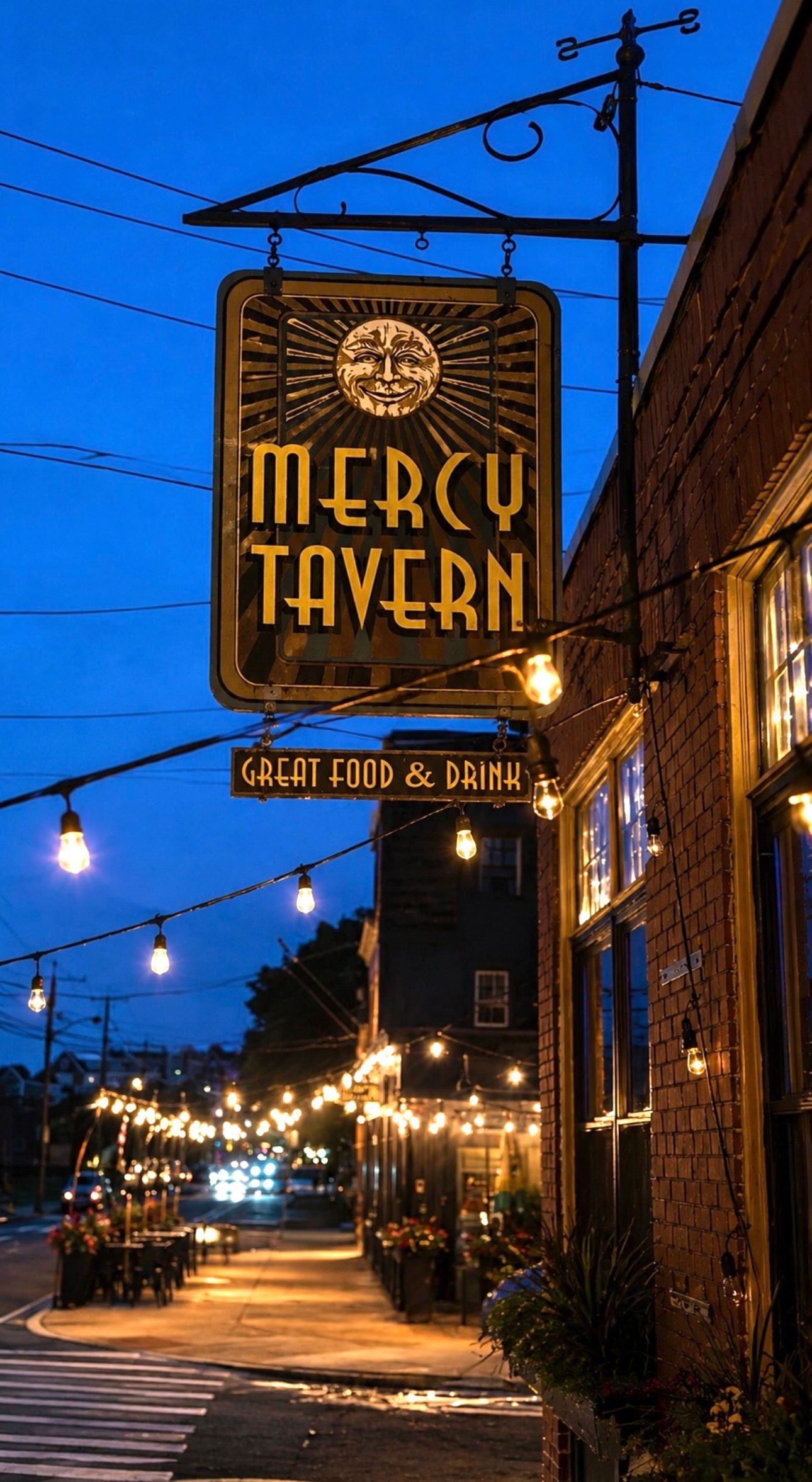The illuminated Art Deco Mercy Tavern sign and string lights on Derby Street in Salem at blue hour