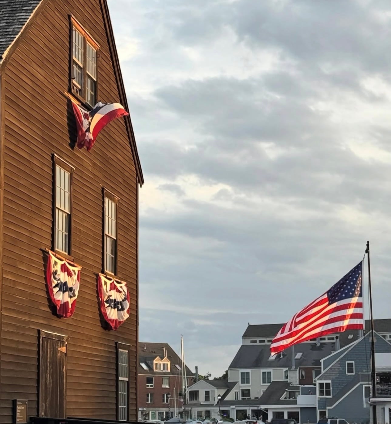 A historic wooden warehouse draped in patriotic bunting at Salem Maritime, an American flag flying at golden hour