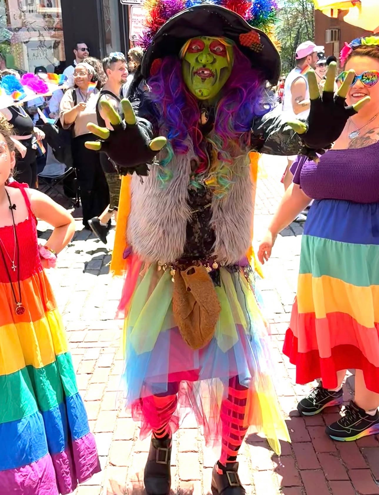 Borah the Witch — a person in an elaborate green-faced witch costume with rainbow hair and a rainbow tulle skirt — at Salem Pride on a downtown brick street