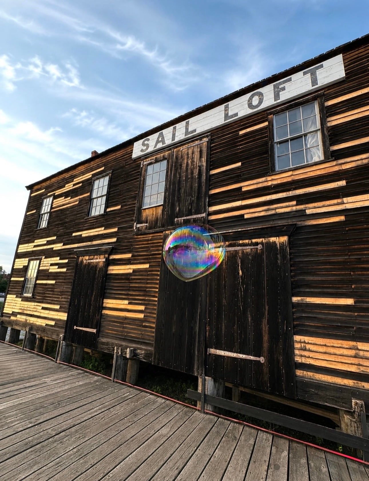 The historic weathered-wood Sail Loft building at Salem Maritime at golden hour, a floating soap bubble in front