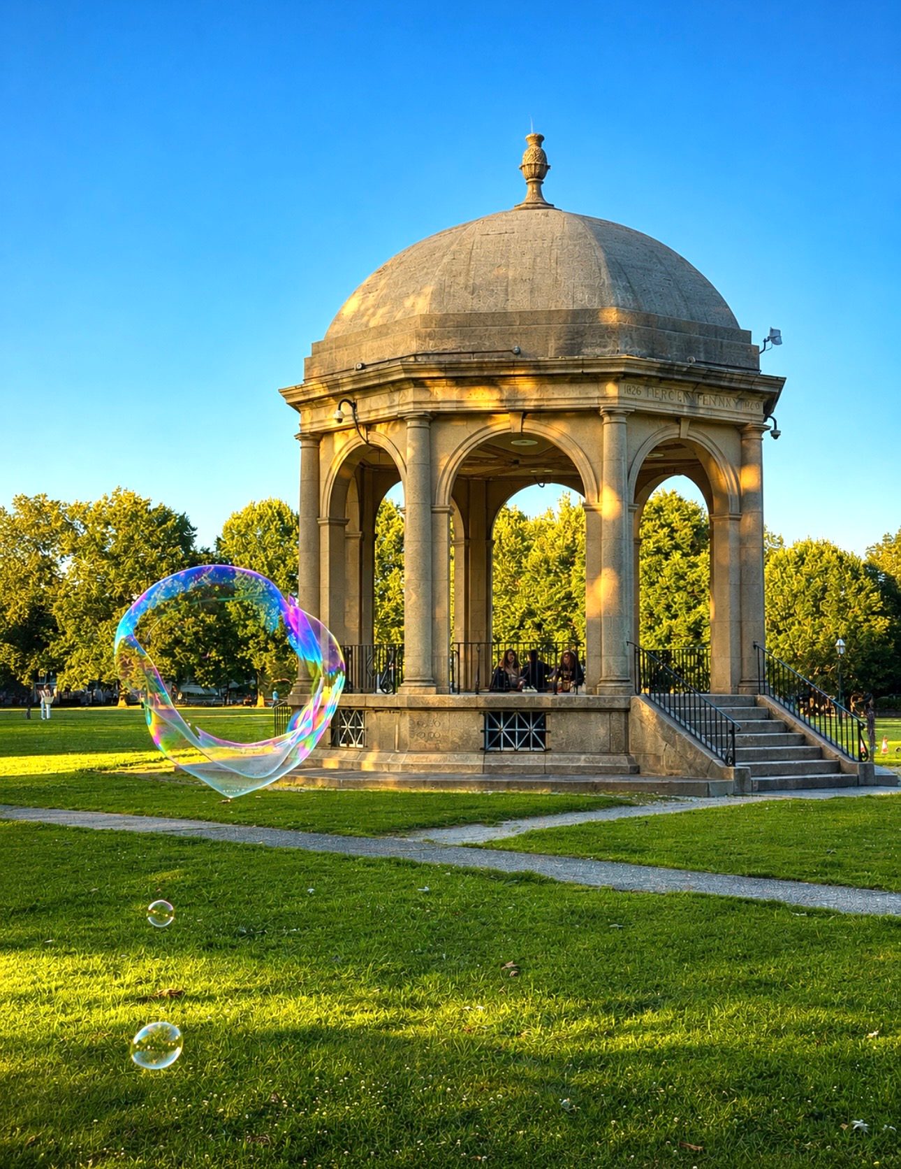 A giant soap bubble drifts past the historic 1926 bandstand on Salem Common at golden hour