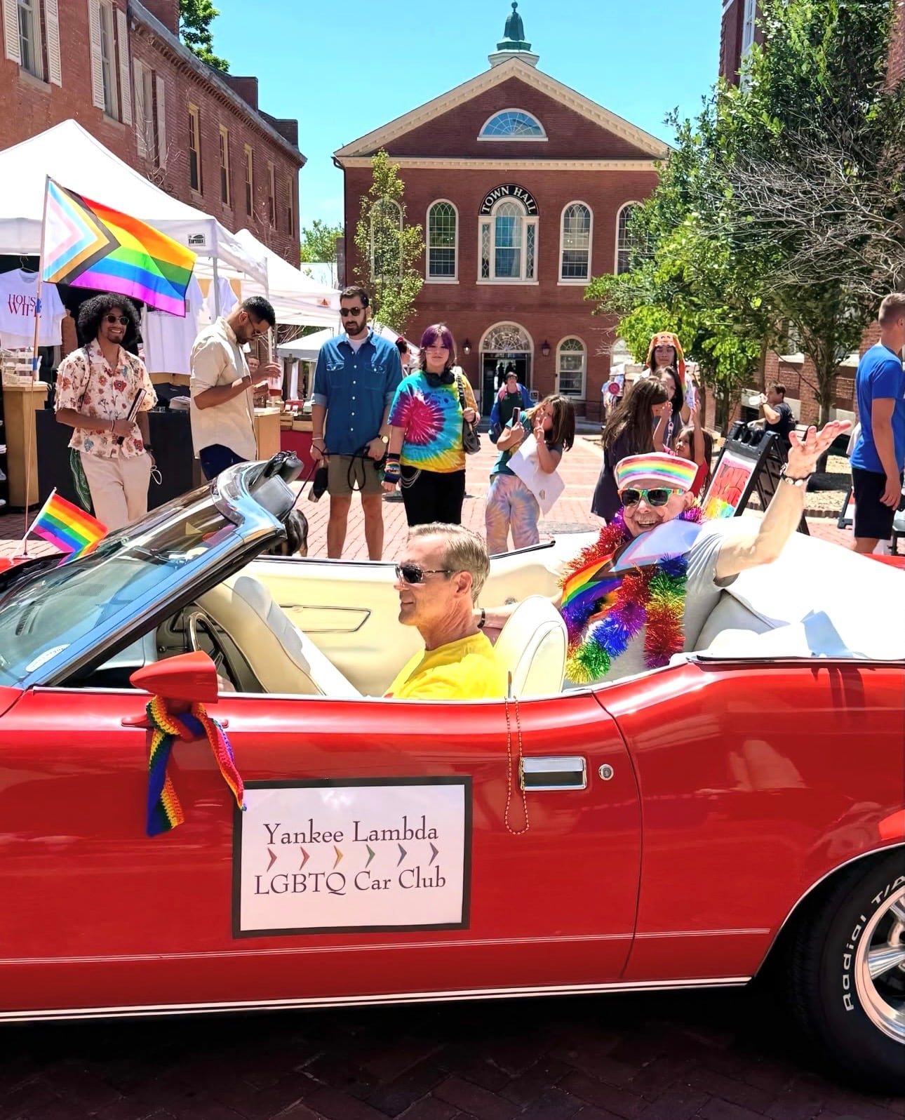 A vintage red convertible from an LGBTQ car club decorated with rainbow flags in front of Old Town Hall in Derby Square during Salem Pride