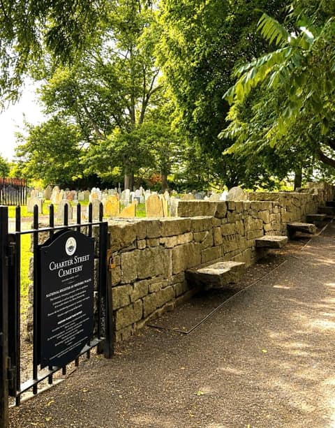 The gated entrance and dry stone wall of Charter Street Cemetery, Salem's oldest burying ground, with colonial slate headstones under summer trees