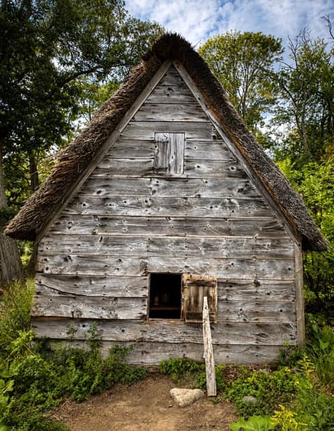 The weathered plank gable end of a thatched cottage with an open shuttered window