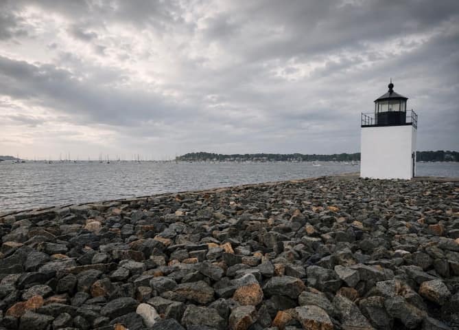 Derby Wharf Light, a small white lighthouse, at the end of a rocky breakwater on Salem Harbor under overcast skies, Salem MA
