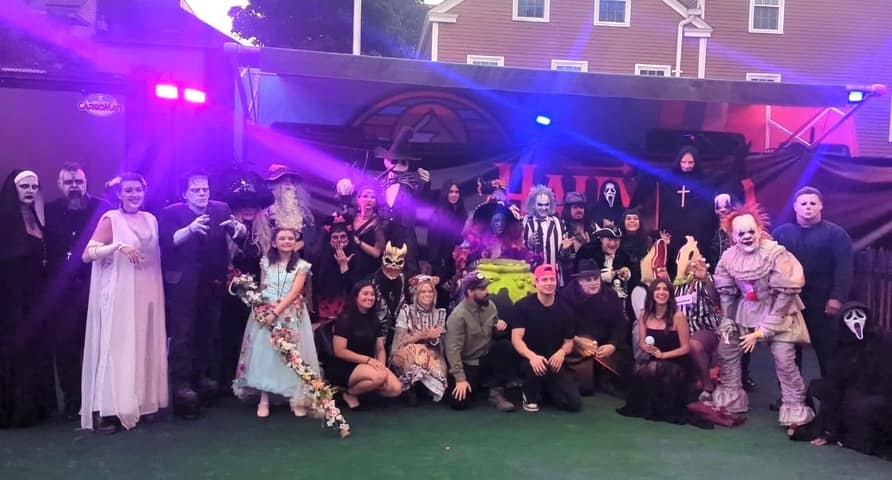 About twenty performers in horror costumes — Frankenstein’s monster, Beetlejuice, Pennywise, Ghostface, Michael Myers, a nun and a witch among them — posed in two rows under purple stage lights