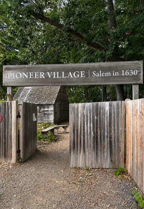 A weathered wooden sign reading “Pioneer Village · Salem in 1630” above an open gate into the village