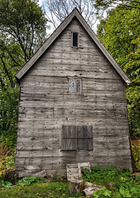 A tall silvered plank gable with a small leaded window high up and a shuttered opening below